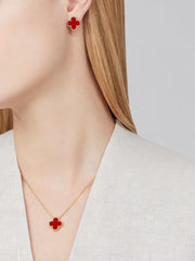Red clover-shaped earrings and necklace on a person against a neutral background