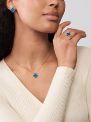 Woman wearing blue clover-shaped earrings and a matching necklace with a neutral background