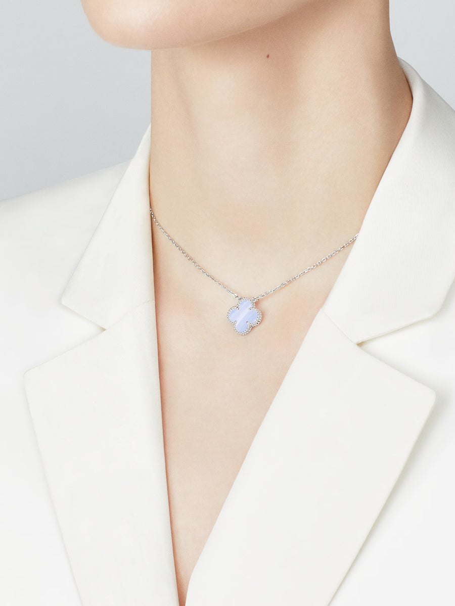 Necklace with a floral pendant worn by a person in a white blazer.