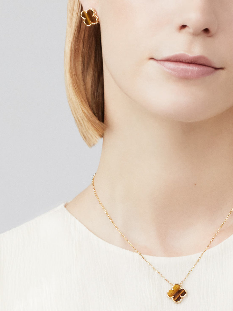 Close-up of a person wearing a gold necklace with a clover-shaped pendant on a light gray background.