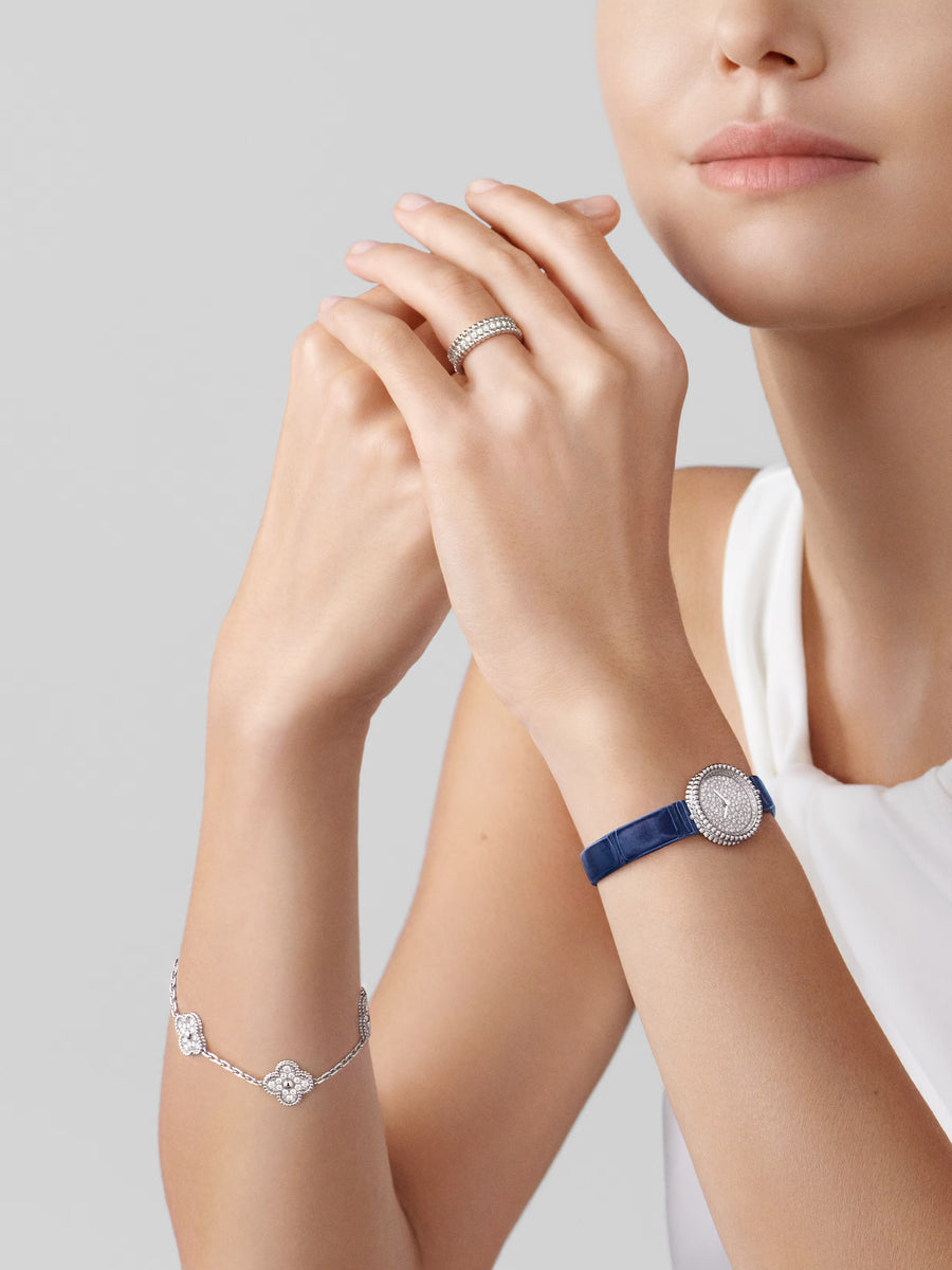 Woman's hands and arm wearing a ring, bracelet, and watch on a light gray background