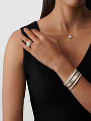 Woman wearing a black dress with silver jewelry including a ring, bracelet, and necklace on a light gray background.