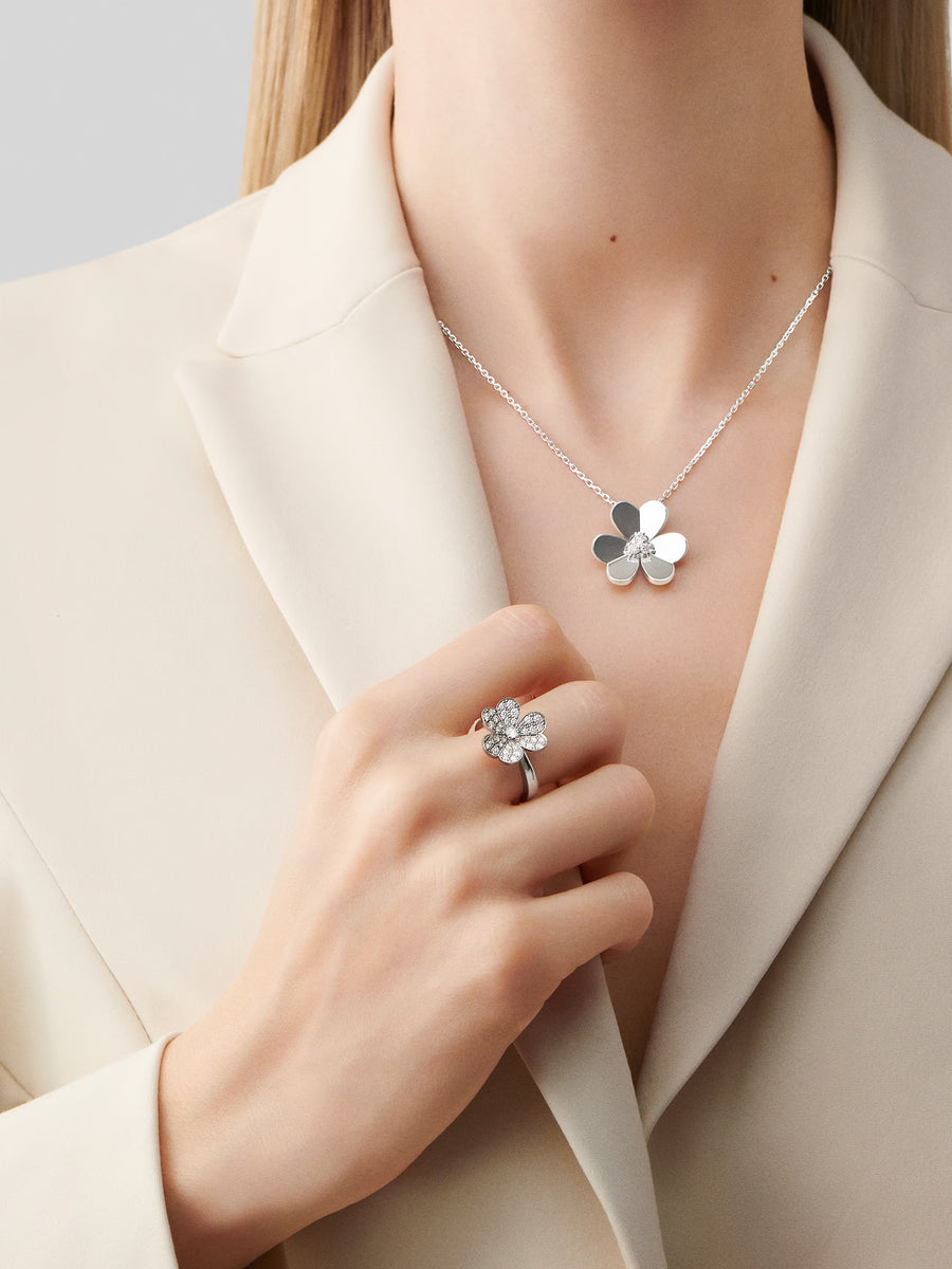 Person wearing a silver necklace with a flower pendant and matching ring on a neutral background