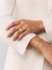 Gold floral ring and bracelet on a hand against a neutral background