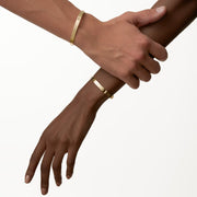 Two hands holding each other with gold bracelets on a white background