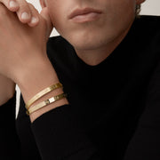 Close-up of a person wearing two gold bracelets on a plain background