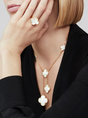 Woman wearing a gold necklace with white floral pendants and matching ring.
