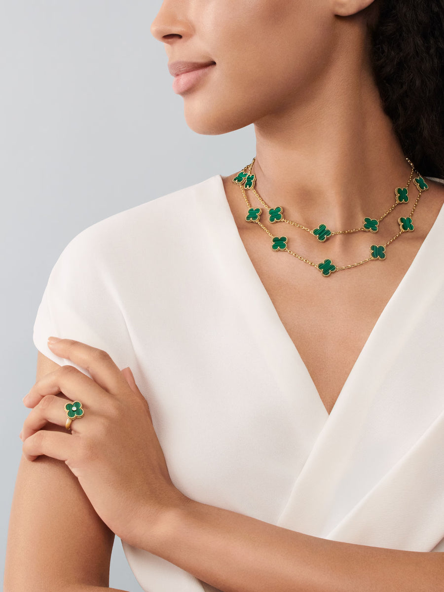 Woman wearing a gold necklace with green clover pendants and matching ring on a plain background