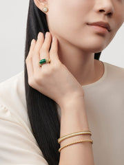 Woman wearing gold jewelry including earrings, ring, and bracelets on a neutral background