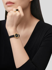 Woman wearing a black watch with gold accents on a plain background