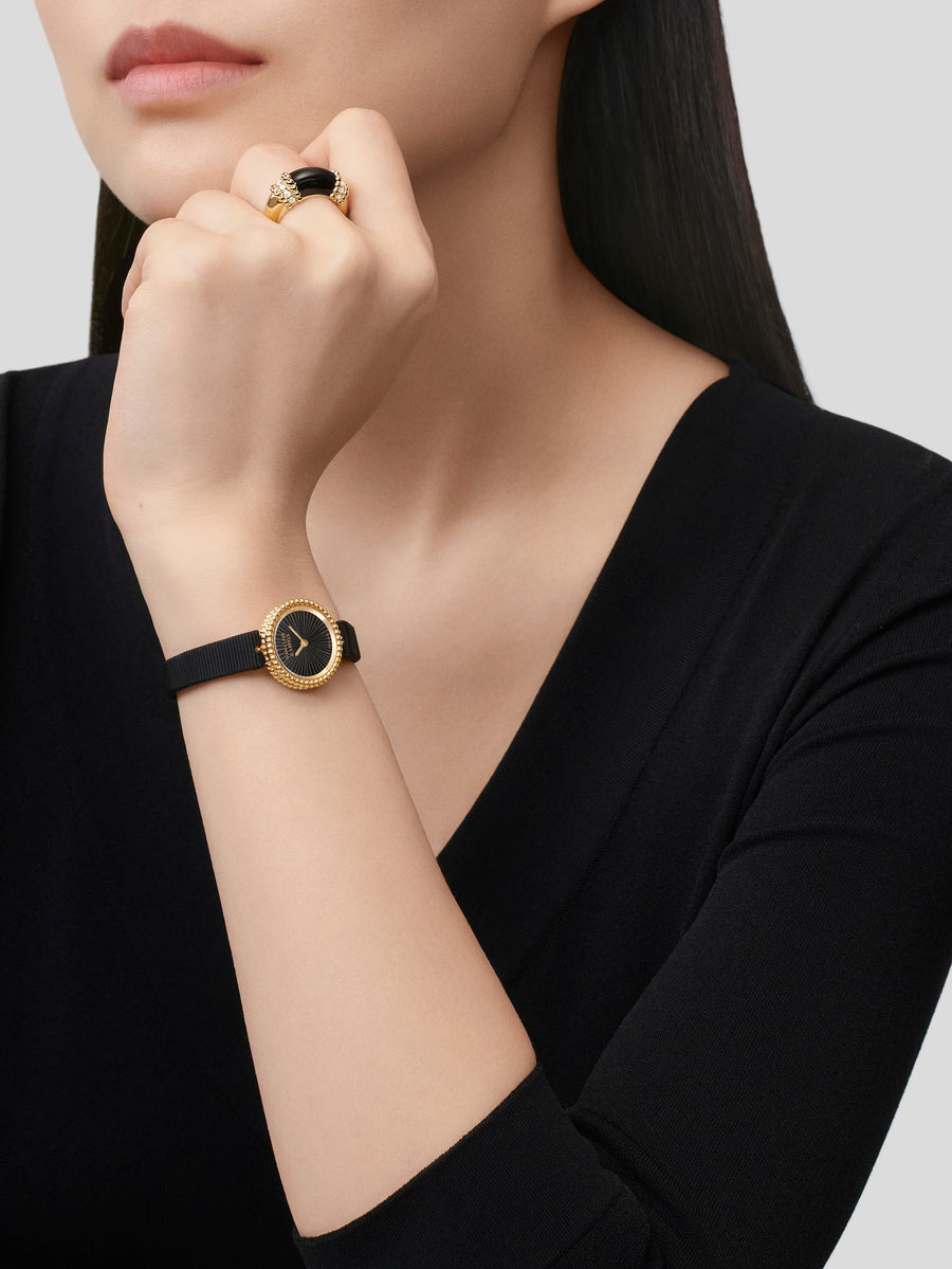 Woman wearing a black watch with gold accents on a plain background