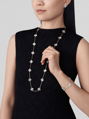 Woman wearing a black dress with silver jewelry including a necklace, bracelet, and earrings on a light gray background.