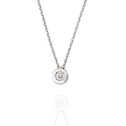 Close-up of bezel-set moissanite pendant in white gold on reflective surface