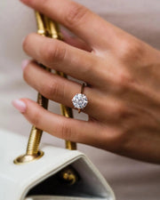 The Brittany 3.5ct Moissanite ring in yellow gold worn on hand holding perfume bottle