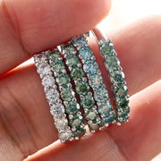 Stack of coloured Moissanite rings worn on hand – blue, green, and white stones