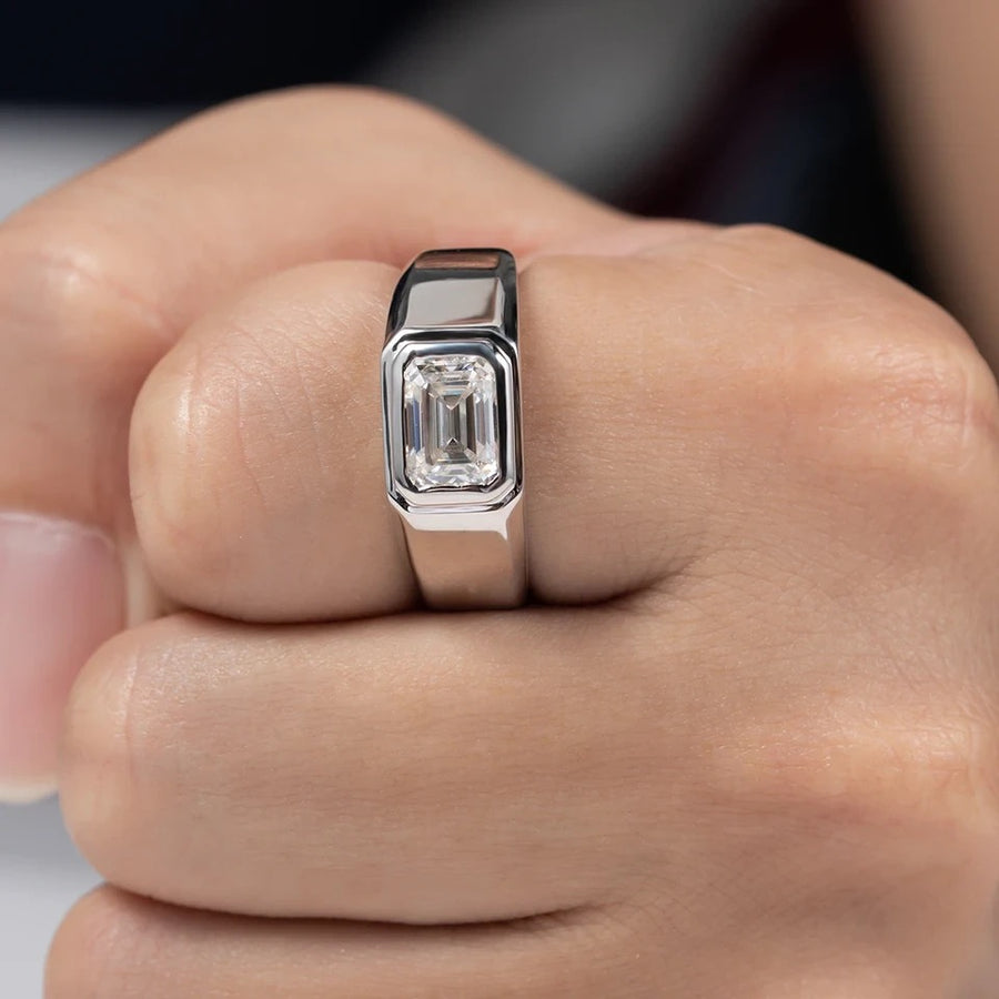 A man's ring with a silver band and a central emerald cut moissanite stone.