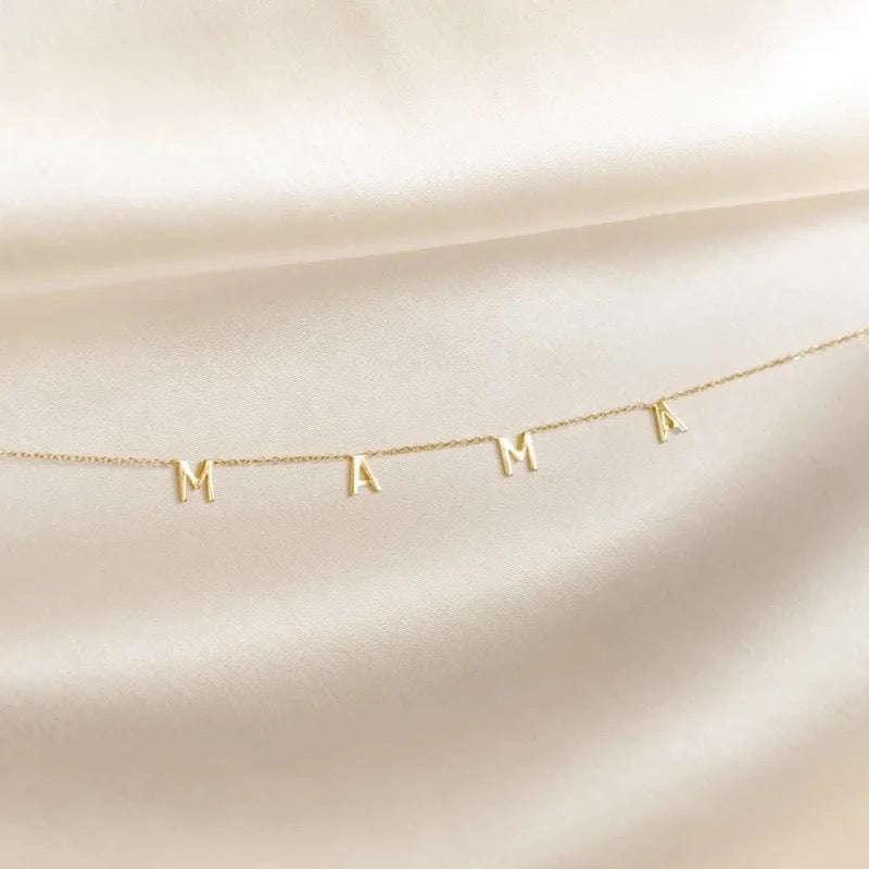 A gold vermeil necklace with the letter 'M' on a sterling silver chain, displayed against a white fabric background.