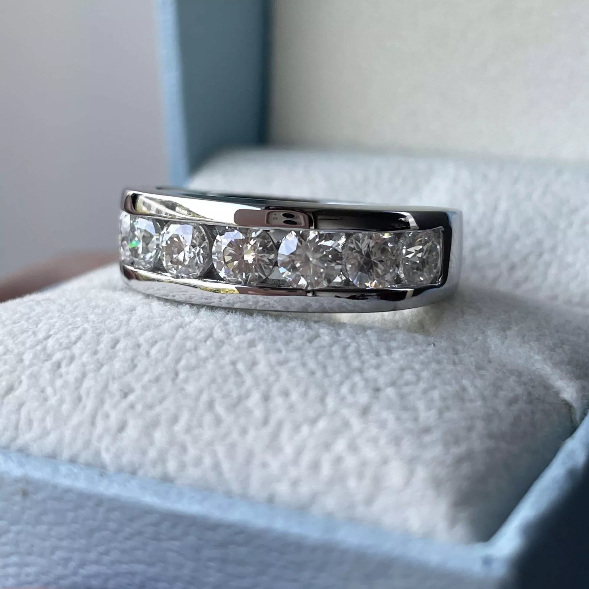 A men's silver and white gold ring with multiple emerald cuts on a white card in a blue box.