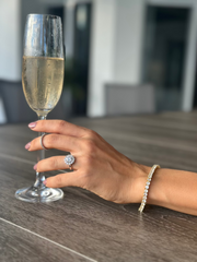 Woman wearing Soho 4mm Moissanite Tennis Bracelet in gold, holding a champagne glass – elegant and sparkling