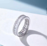 A white gold plated 925 silver baguette and round stacking ring with moissanites set on it, placed on a blue background.