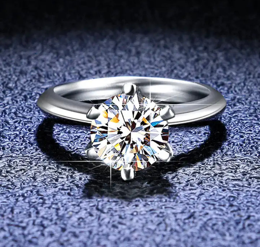 A 1ct round solitaire Moissanite ring set in a silver band, showcasing a clear and sparkling stone.