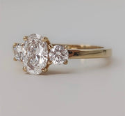 An oval ice cut Moissanite ring with two round side moissanites set in a yellow gold band.