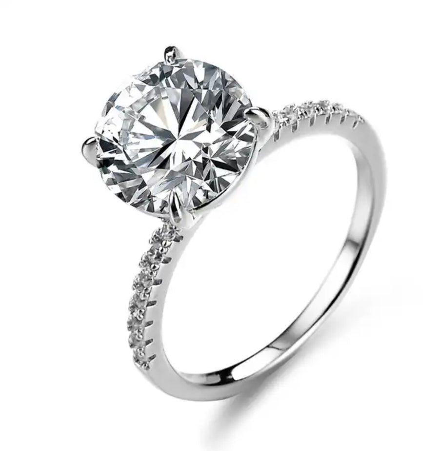 A silver-colored Moissanite diamond ring with a single stone set on a classic four-clawed base.