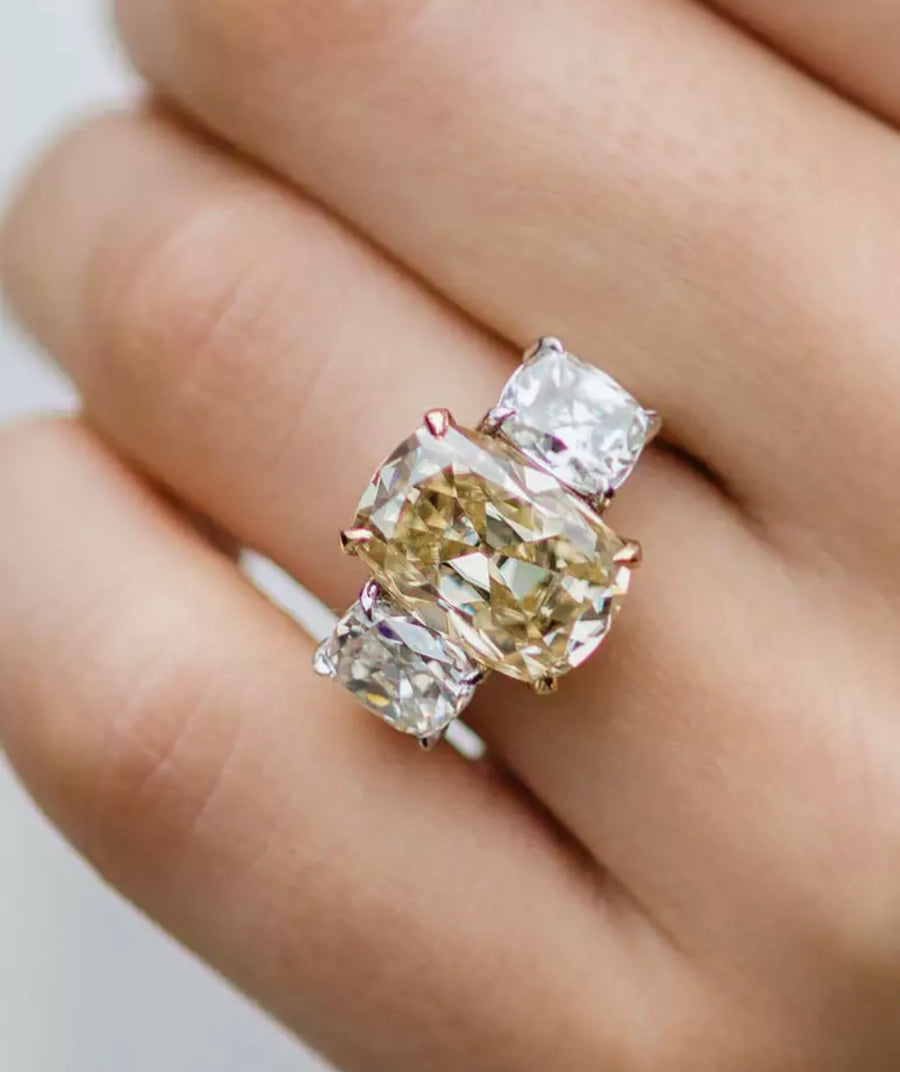 A hand holding a sparkling 7ct Old Mine Cut Moissanite ring with a soft Canary yellow color, set in a white gold band.