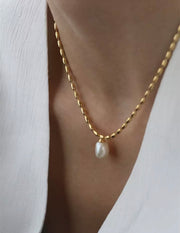 A close-up image of a gold-colored pearl pendant necklace with a chain.