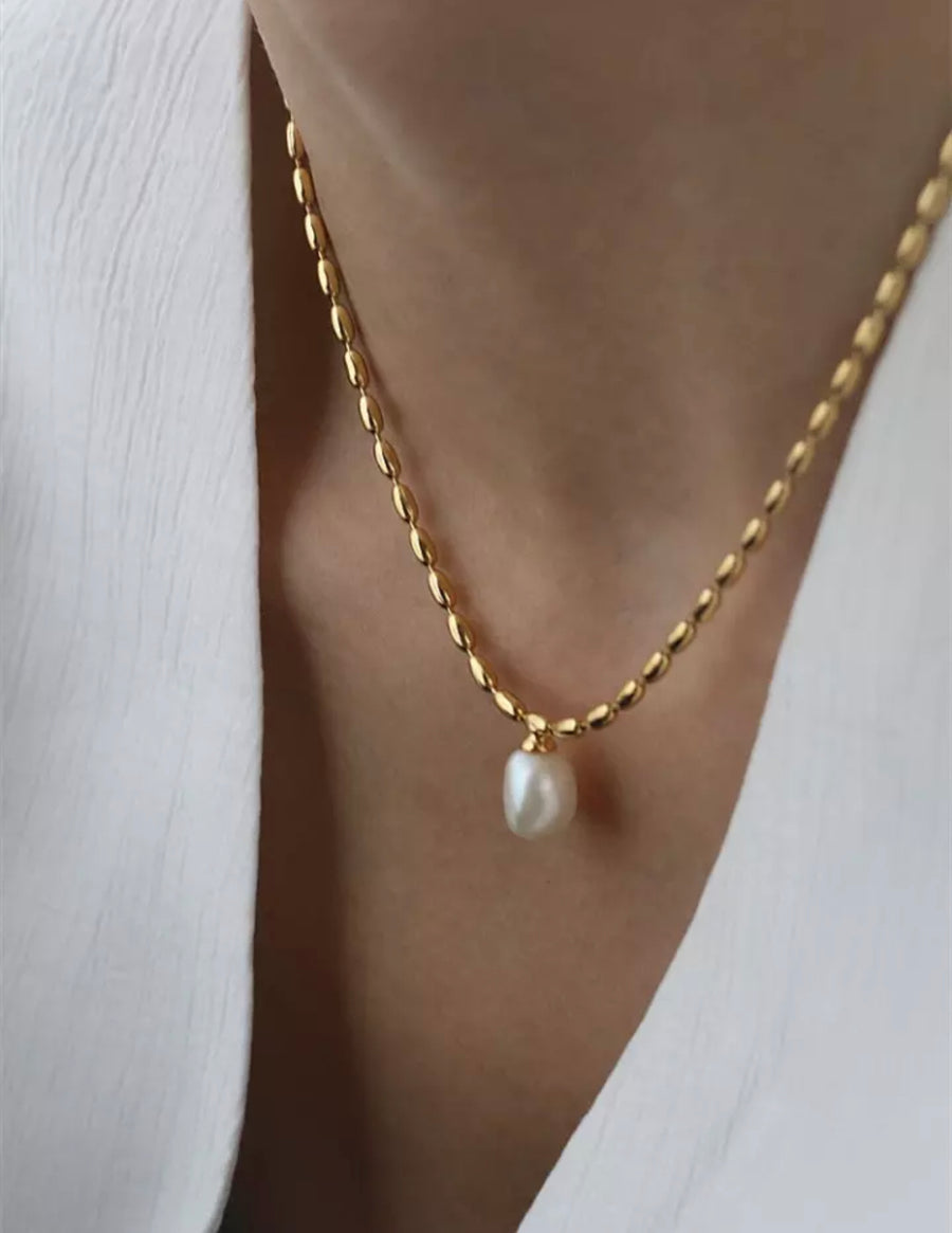 A close-up image of a gold-colored pearl pendant necklace with a chain.