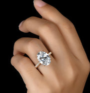 A hand holding a 5ct moissanite ring with a white gold plating and a halo design