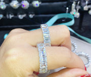 A hand displaying a large emerald-cut moissanite ring with multiple smaller stones set around it, possibly a piece of jewelry.