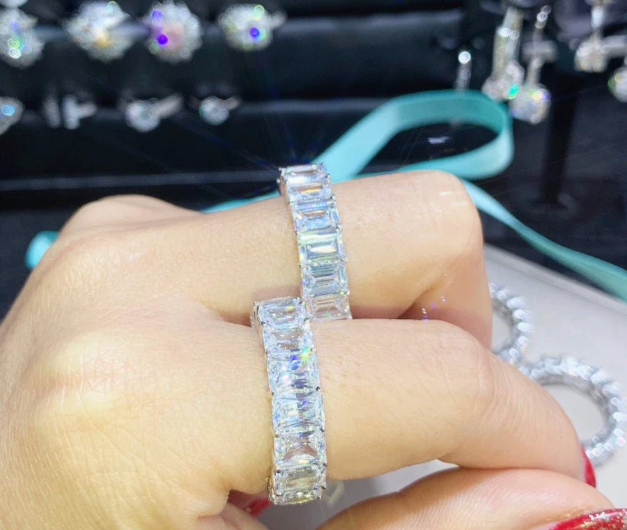 A hand displaying a large emerald-cut moissanite ring with multiple smaller stones set around it, possibly a piece of jewelry.