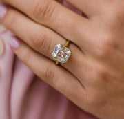 A hand holding a 4.5ct asscher cut Moissanite ring with a gold plating, Solid 10k white gold version.