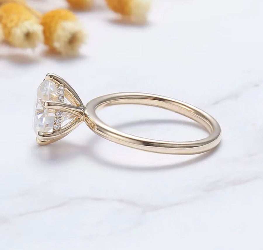 A gold ring with a clear, round Moissanite gemstone in the center, placed on a white marble surface with corn flakes in the background.