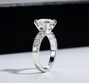 A silver ring with a central moissanite stone and smaller stones set in a pave around the band, displayed against a black background.