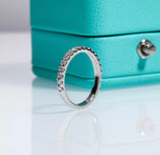 Close-up of a white gold pavé Moissanite wedding band standing upright in front of a teal jewellery box