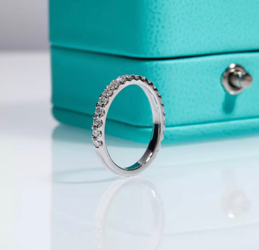 Close-up of a white gold pavé Moissanite wedding band standing upright in front of a teal jewellery box