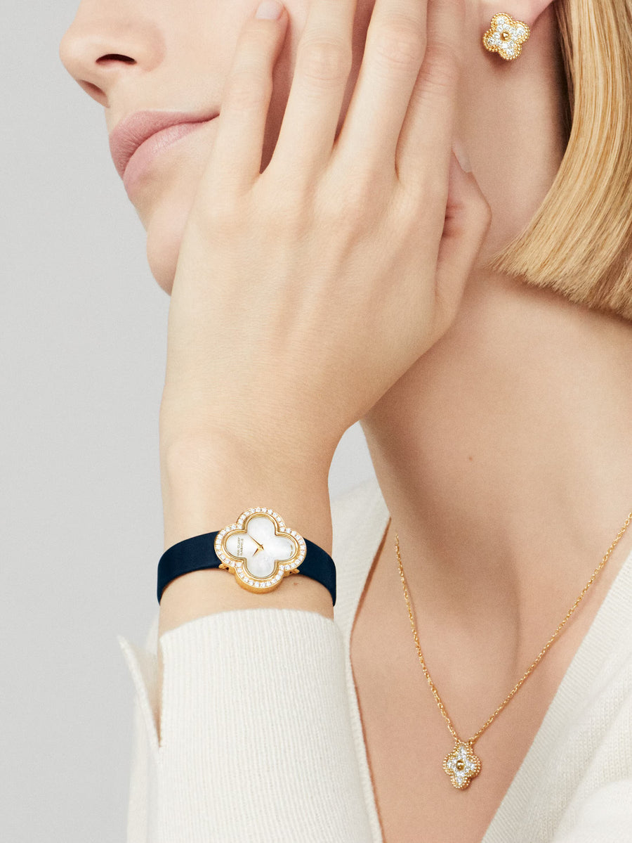 Close-up of a person wearing a gold necklace, bracelet, and earrings with a neutral background
