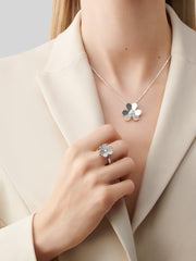 Person wearing a silver necklace with a flower pendant and matching ring on a neutral background