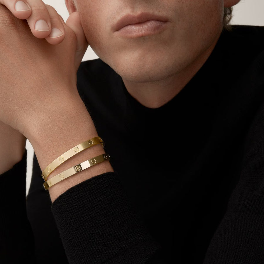 Close-up of a person wearing two gold bracelets on a plain background