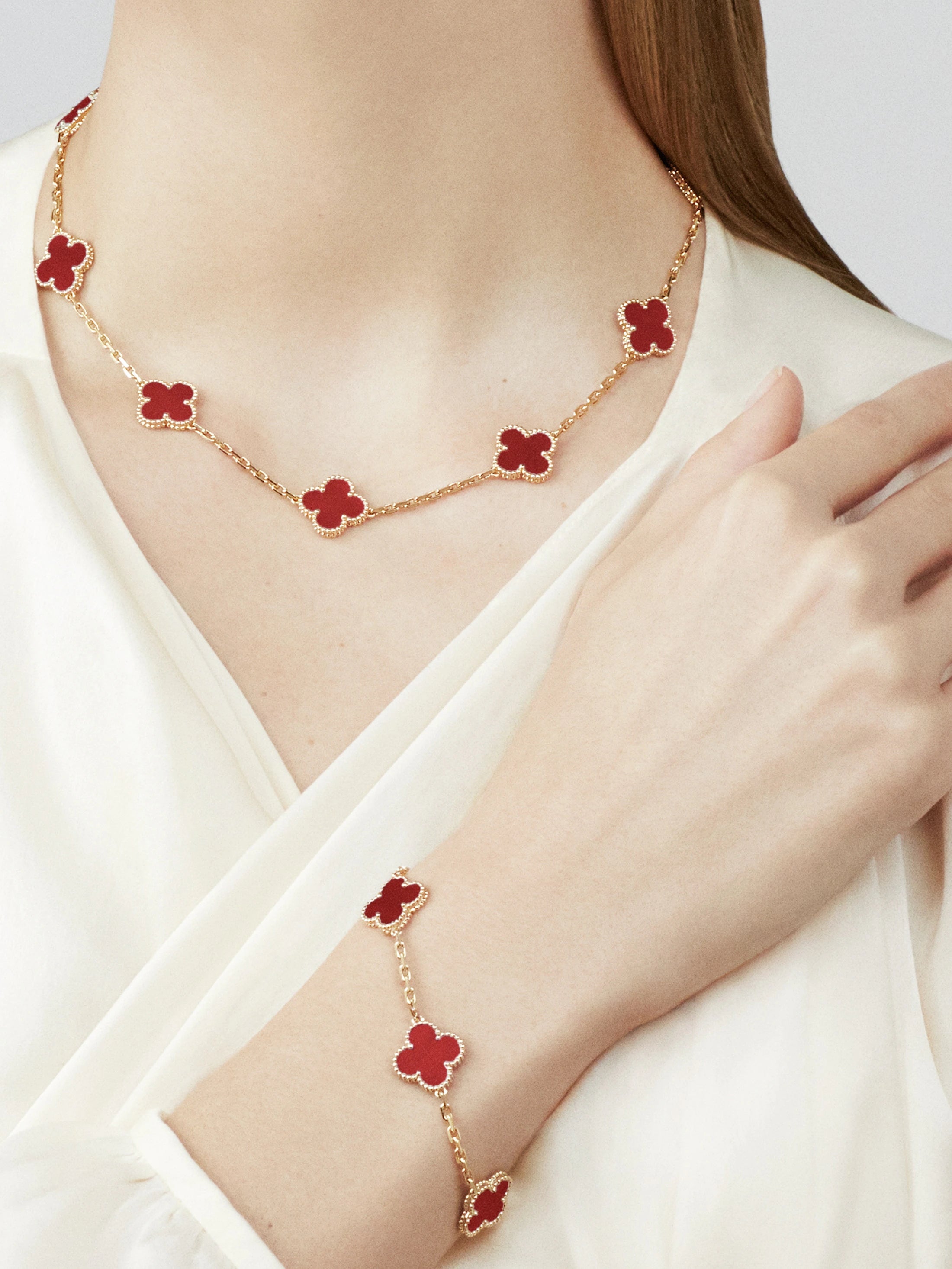 Gold necklace with red flower pendants worn by a person on a white background
