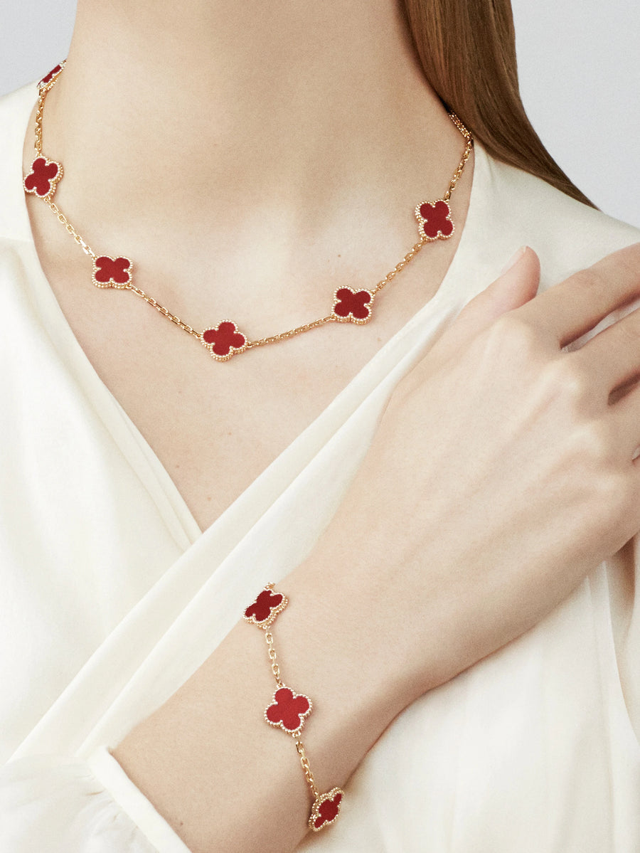 Gold necklace with red flower pendants worn by a person on a white background