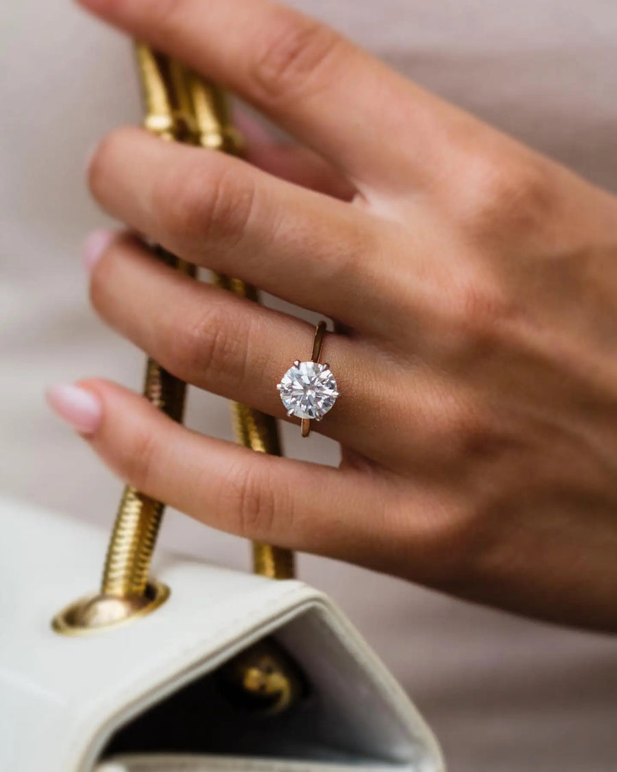 The Brittany 3.5ct Moissanite ring in yellow gold worn on hand holding perfume bottle