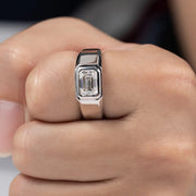 A man's ring with a silver band and a central emerald cut moissanite stone.
