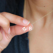 A gold vermeil pendant initial letter necklace with a sterling silver chain, held between fingers, showcasing the letter 'B'.