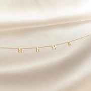 A gold vermeil necklace with the letter 'M' on a sterling silver chain, displayed against a white fabric background.