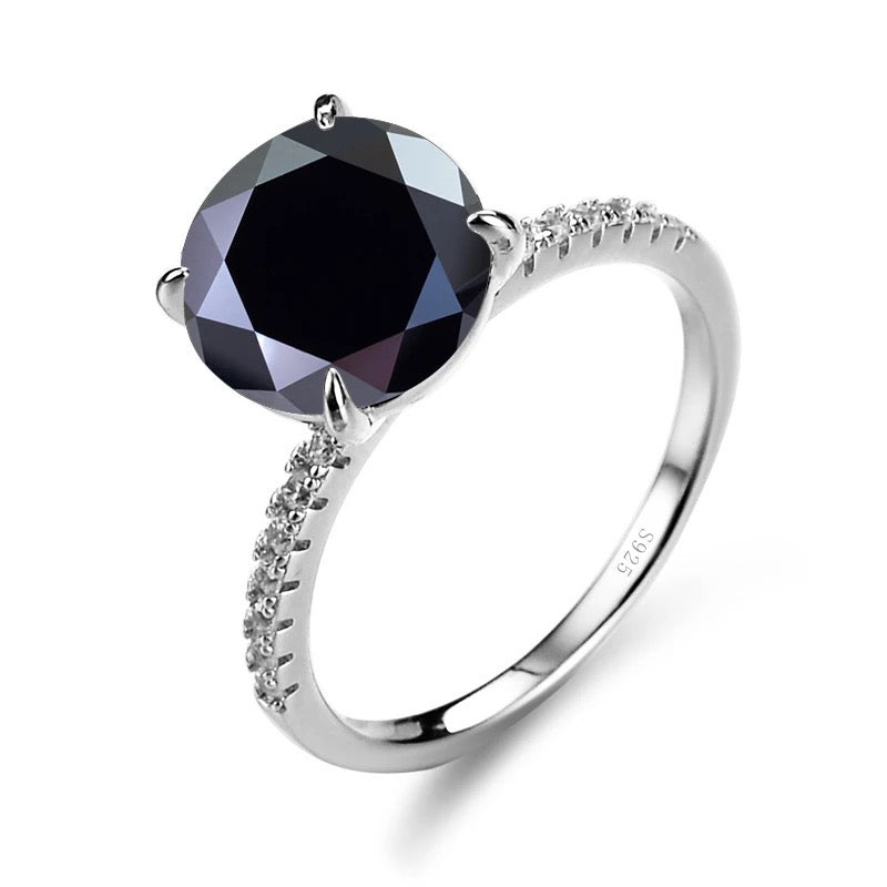 A silver ring with a central black moissanite stone surrounded by smaller clear stones set in a classic four-clawed setting.