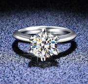 A 1ct round solitaire Moissanite ring set in a silver band, showcasing a clear and sparkling stone.