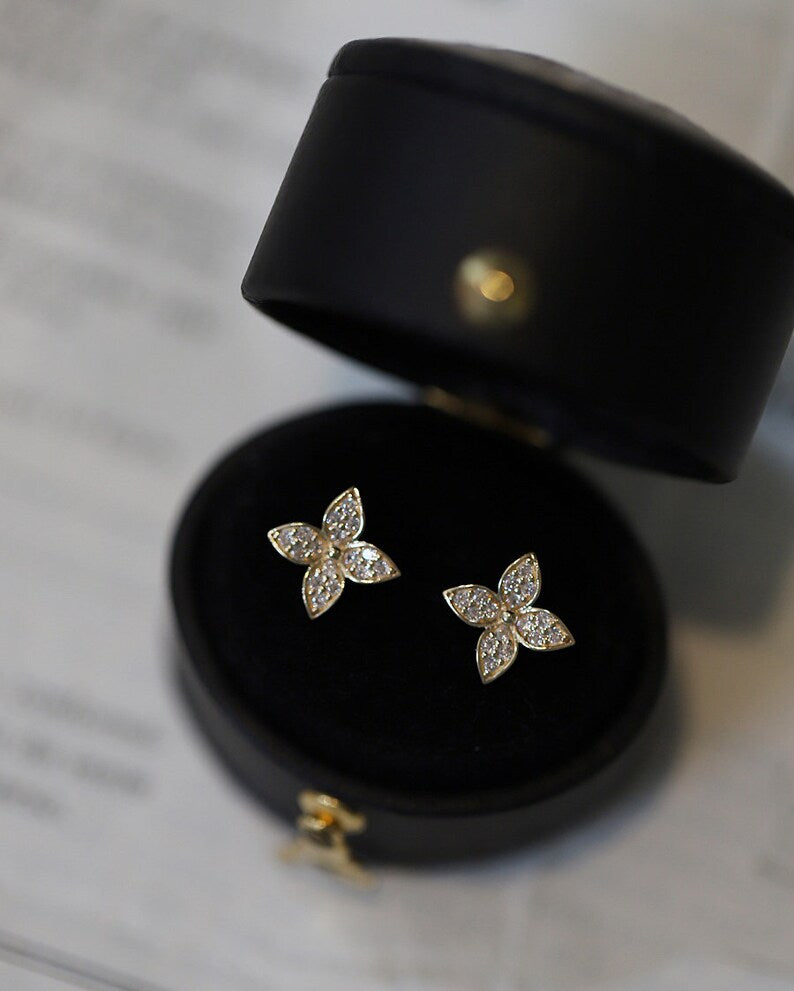 A pair of gold plated flower earrings in a black case, showcasing the earrings' design and the reflection of the earrings on the inner surface of the case.